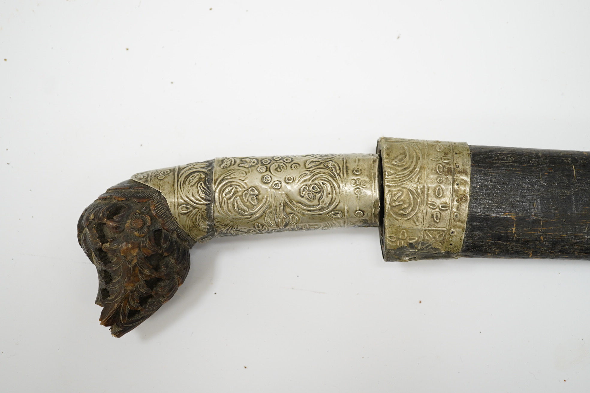 A Malaysian sword Parang, with broad curved pattern welded single edged blade, carved horn pommel, and embossed nickel mounts, in its wooden scabbard. Condition - good